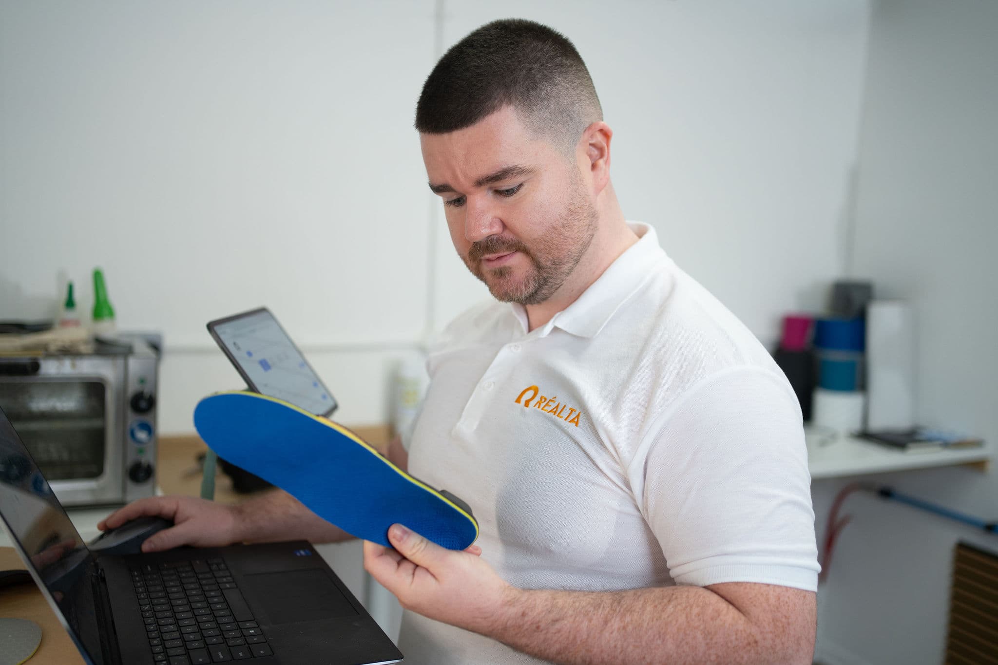 Paul at laptop in workshop holding a blue orthotic shell